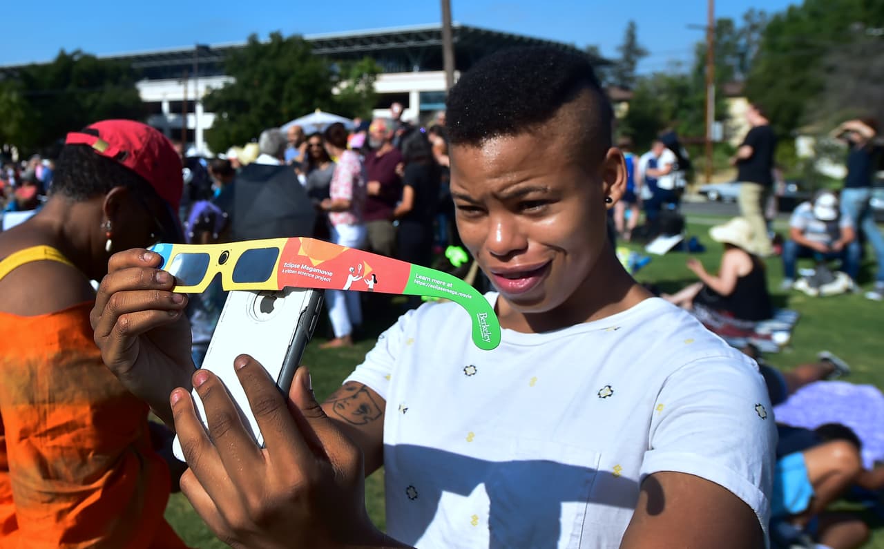 Asha Moore usa los lentes de eclipse en Pasadena para mostrarle a través de su teléfono el fenómeno a un amigo en Canadá.