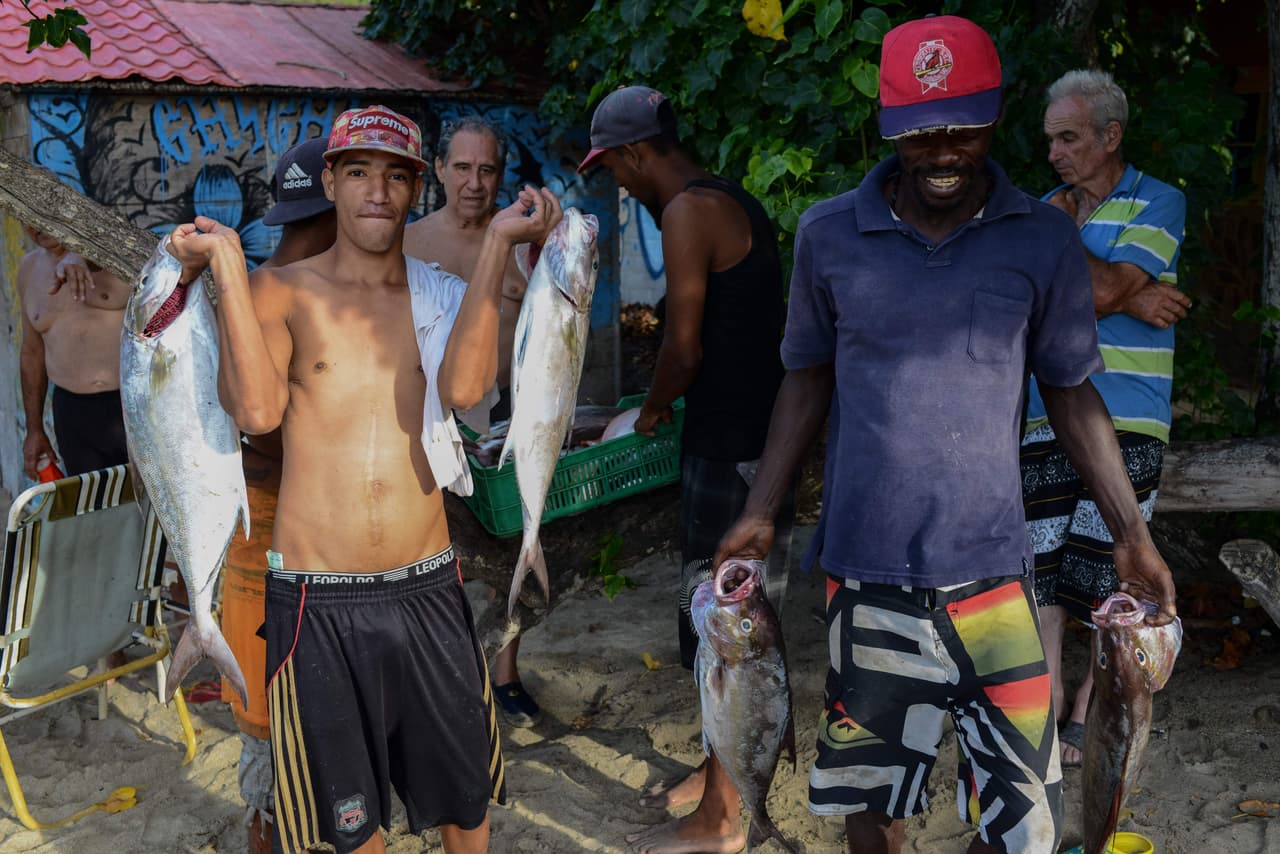 Los pescadores de Chichiriviche de la Costa, un pequeño pueblo turístico a unas 40 millas de Caracas, cargan su mercancía por la playa mientras buscan clientes con suficiente efectivo para poderles comprar. El presidente Nicolás Maduro atribuye la crisis del papel moneda a las mafias que acumulan billetes para especular; la economista Tamara Herrera hace responsable de ello a la hiperinflación y a la emisión de dinero sin respaldo.