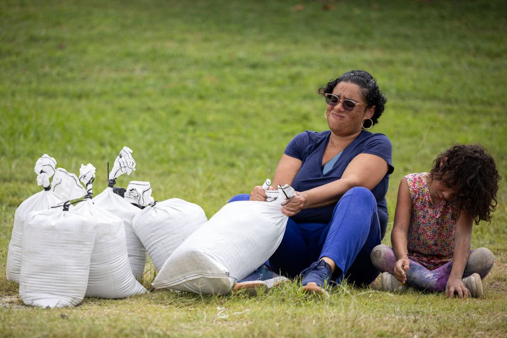 Una niña junto a una mujer llenando los sacos de arena para evitar que las inundaciones afecten sus casas.