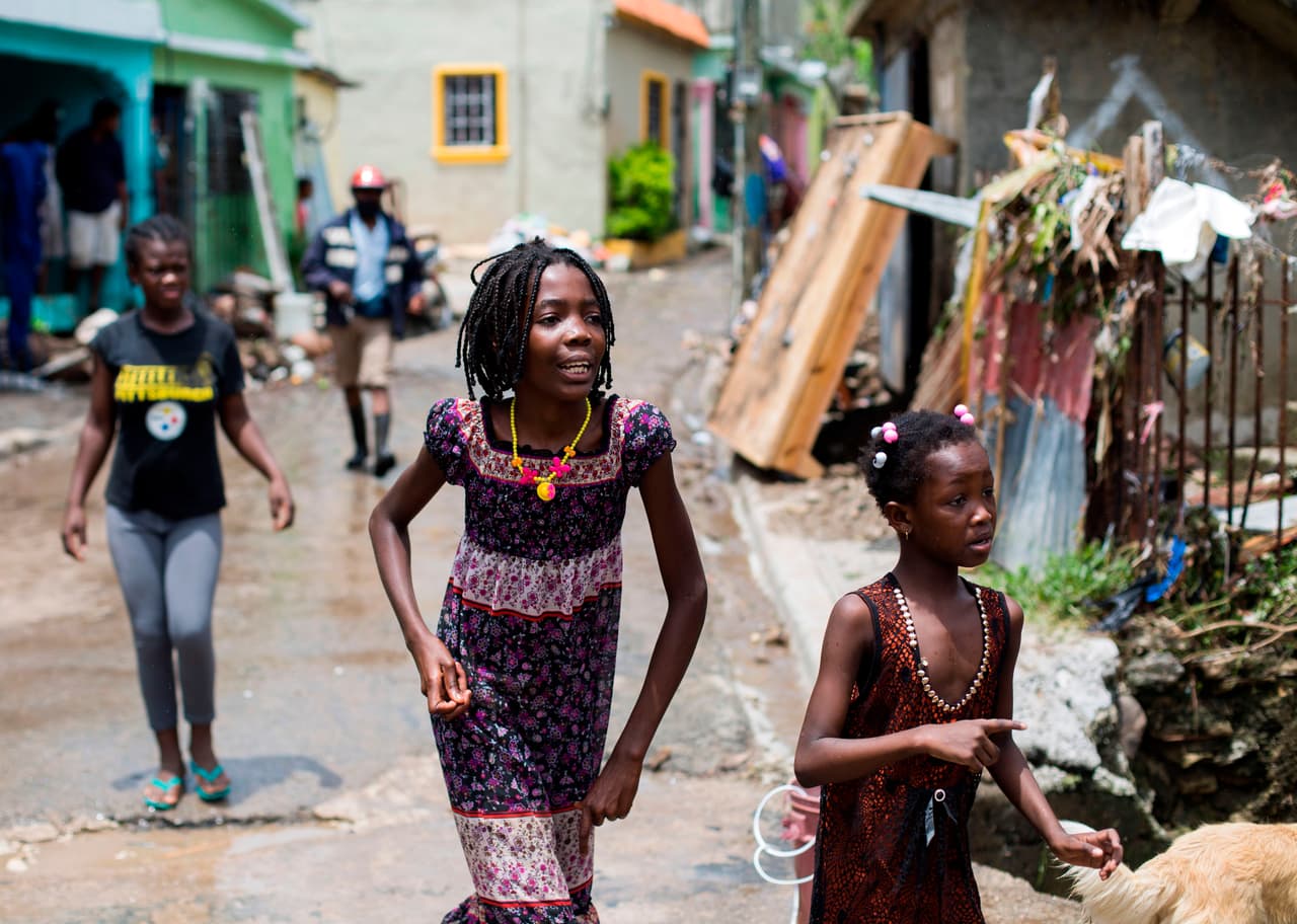 Las niñas corren fuera de su casa dañada después del paso de la tormenta tropical Isaías.