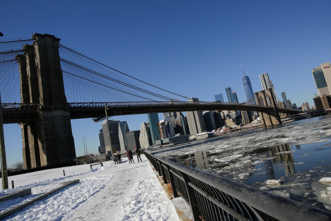 Unas personas miran el hielo flotando a lo largo del East River mientras se divisan los rascacielos de la ciudad de Nueva York, el puente de Brooklyn y el One World Trade Center.