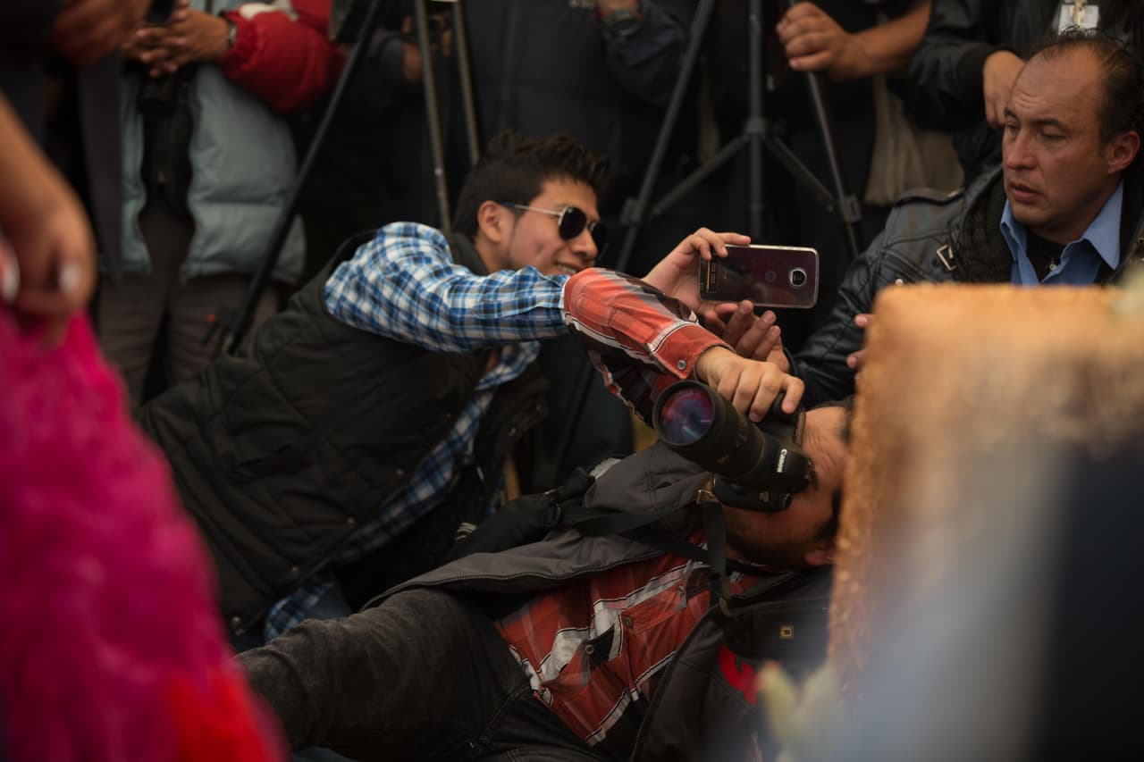 Dos periodistas se trepan en el suelo estirándose para poder tomar una foto de Rubí durante la misa.