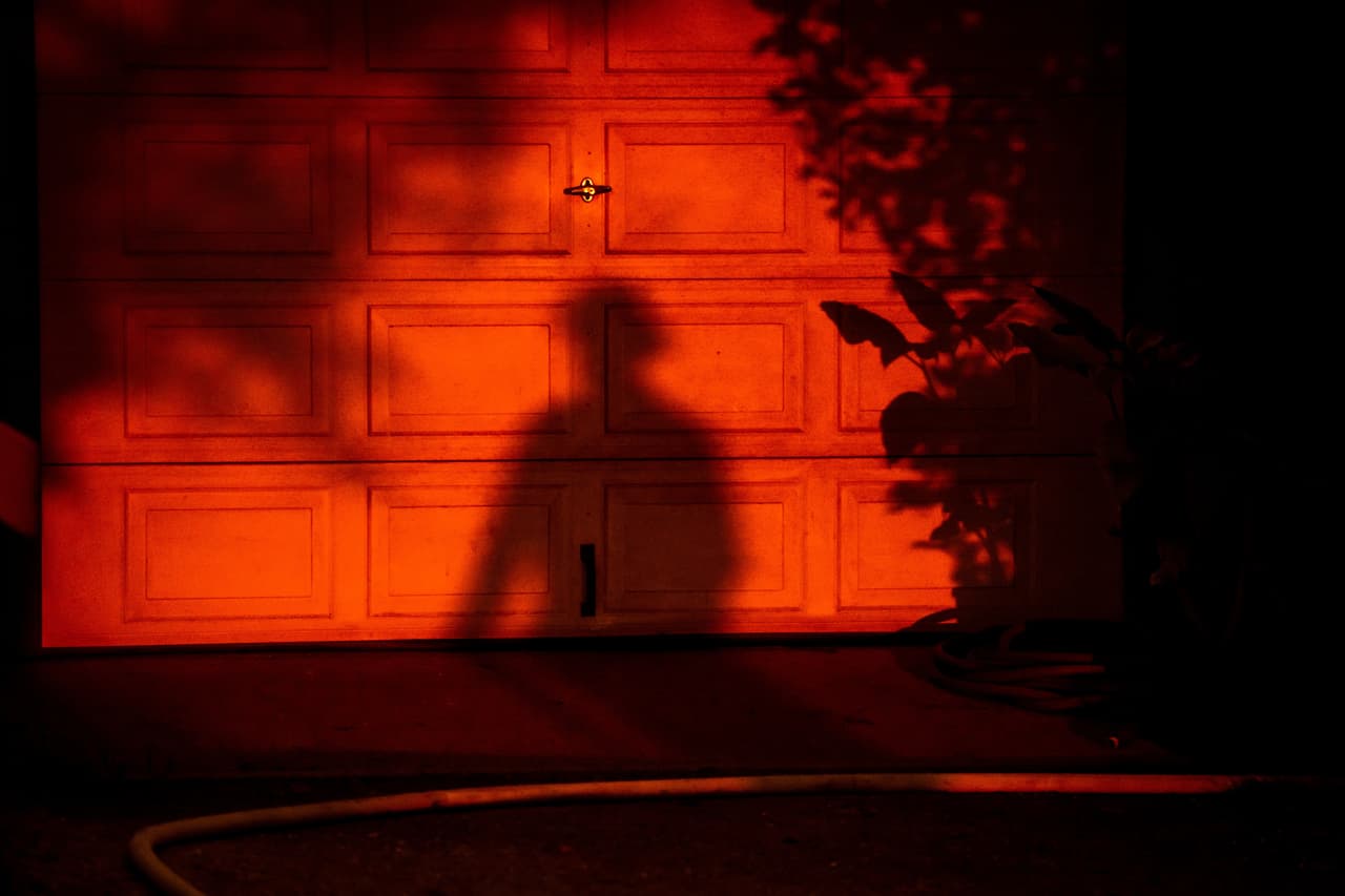 La silueta de un bombero se recorta contra la puerta de un garaje en una propiedad que está siendo protegida del avance del incendio Plaskett, el 28 de agosto de 2026, en Big Sur, California. (AP Foto/Ethan Swope)