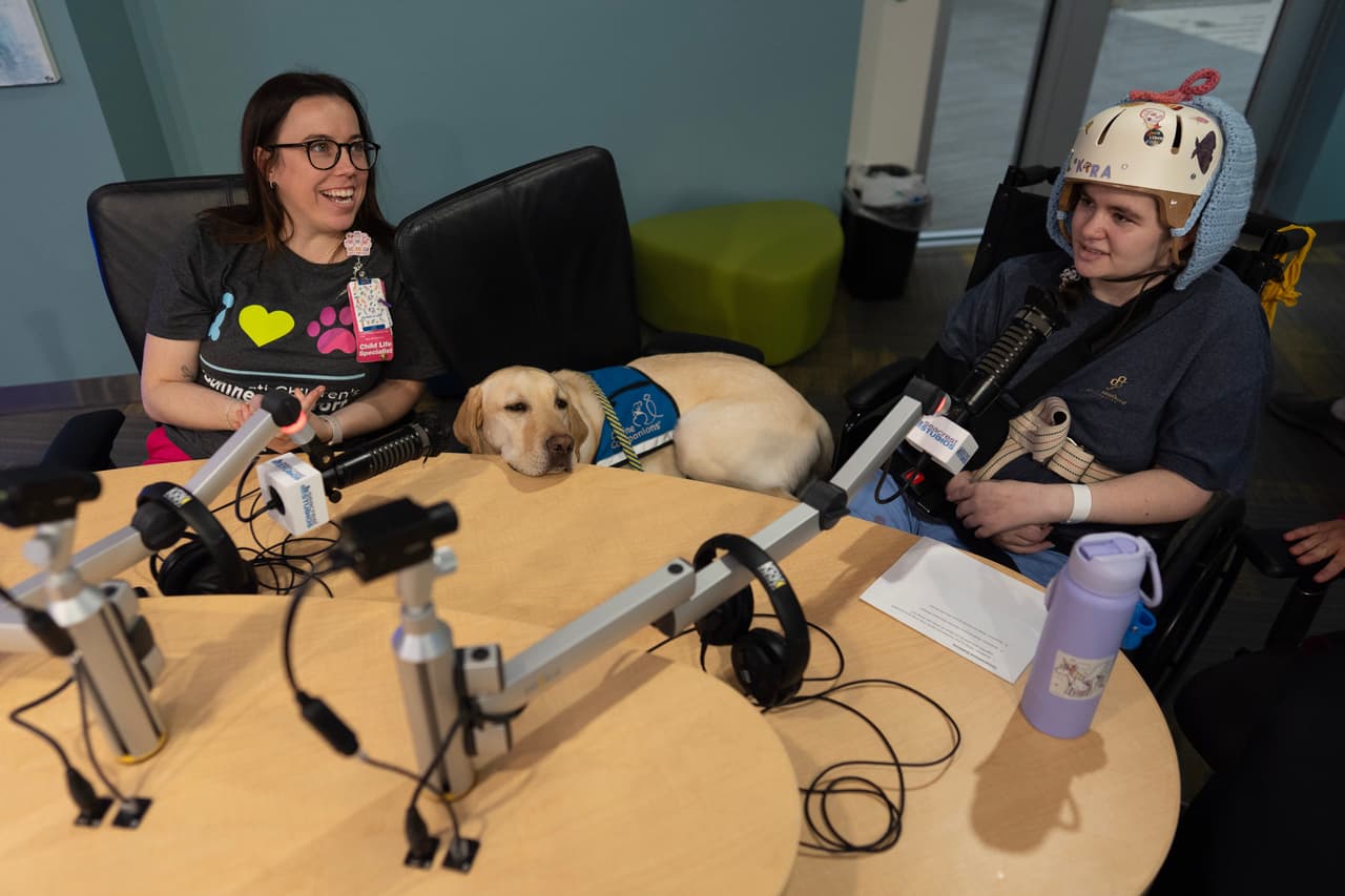 Maggie O'Grady, especialista en atención infantil del Hospital Infantil de Cincinnati (izquierda), y Grover, el perro de terapia del hospital (centro), trabajan con la paciente Kira Hodge en los estudios Seacrest del hospital para producir un programa de televisión de circuito cerrado que se transmite a las habitaciones de los pacientes, en el Hospital Infantil de Cincinnati, el lunes 4 de mayo de 2026