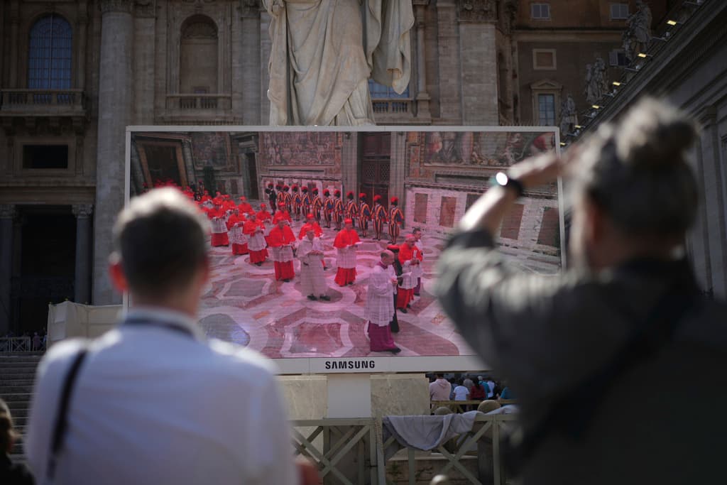 Los fieles observan las imágenes del cónclave hoy, miércoles 7 de mayo de 2025, en una pantalla gigante que muestra a los cardenales entrando al cónclave, en la Plaza de San Pedro del Vaticano.