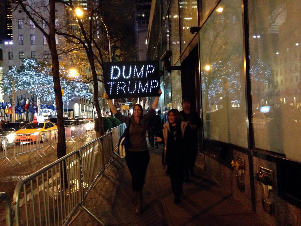 Una manifestante camina con un cartel luminoso que reza consignas contra Trump