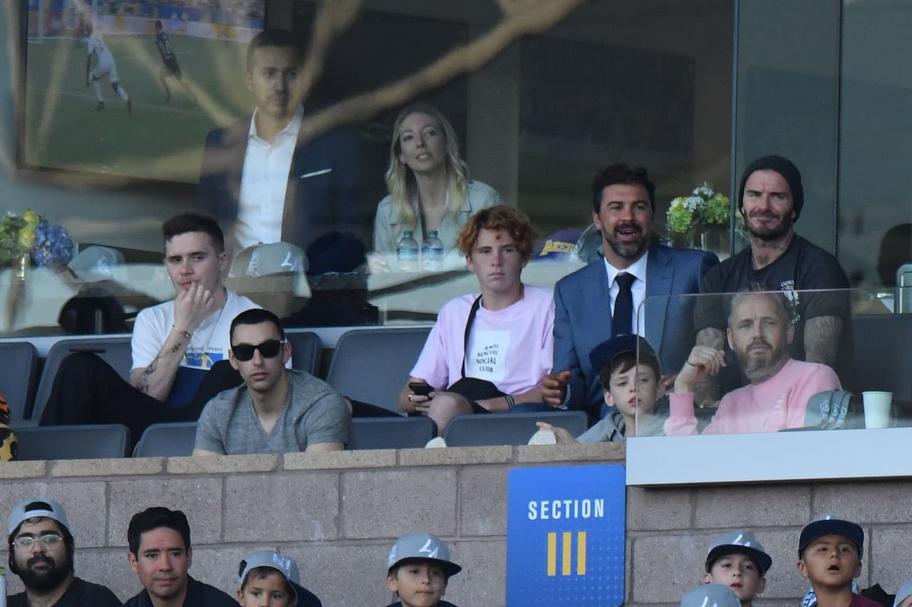 Brooklyn Beckham lució pensativo mientras que su papá y otros amigos (a la derecha) sí disfrutaban de un juego de fútbol.