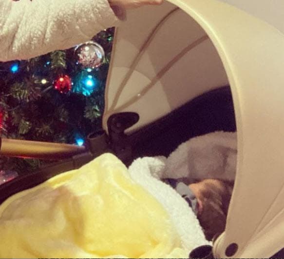La imagen presenta a la pareja con un gesto de sorpresa. Los actores, fotografiados frente a un árbol de Navidad, sostienen copas de vino en sus manos, mientras el pequeño Liam duerme en su cuna.