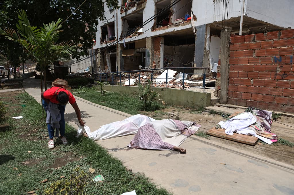 Un hombre intenta reconocer unos cuerpos cubiertos frente a un edificio dañado, en La Guaira, Venezuela.