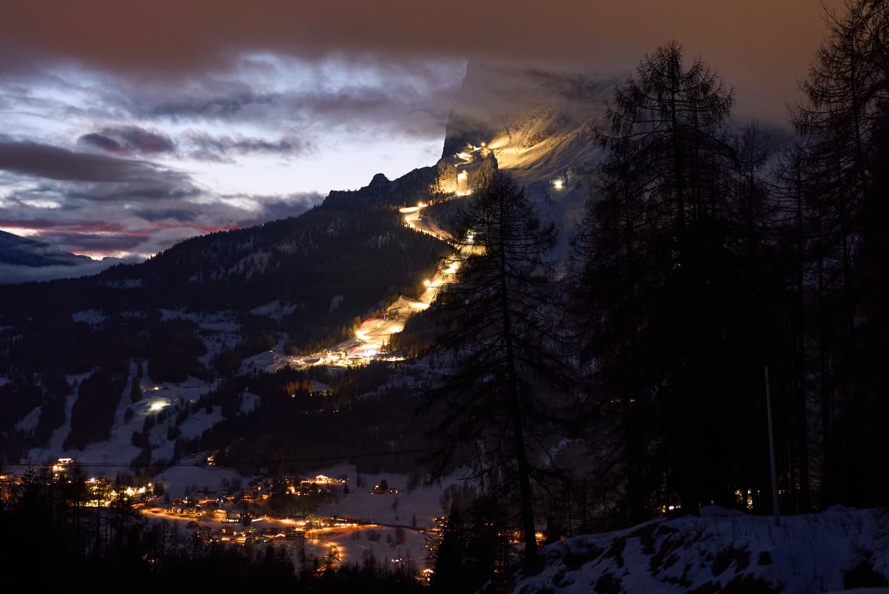 El recorrido de las competiciones olímpicas de esquí alpino femenino se ve iluminado al anochecer, con Cortina d'Ampezzo en primer plano, durante los Juegos Olímpicos de Invierno de 2026, en Cortina d'Ampezzo, Italia, el miércoles 11 de febrero de 2026. (Foto AP/Jacquelyn Martin)