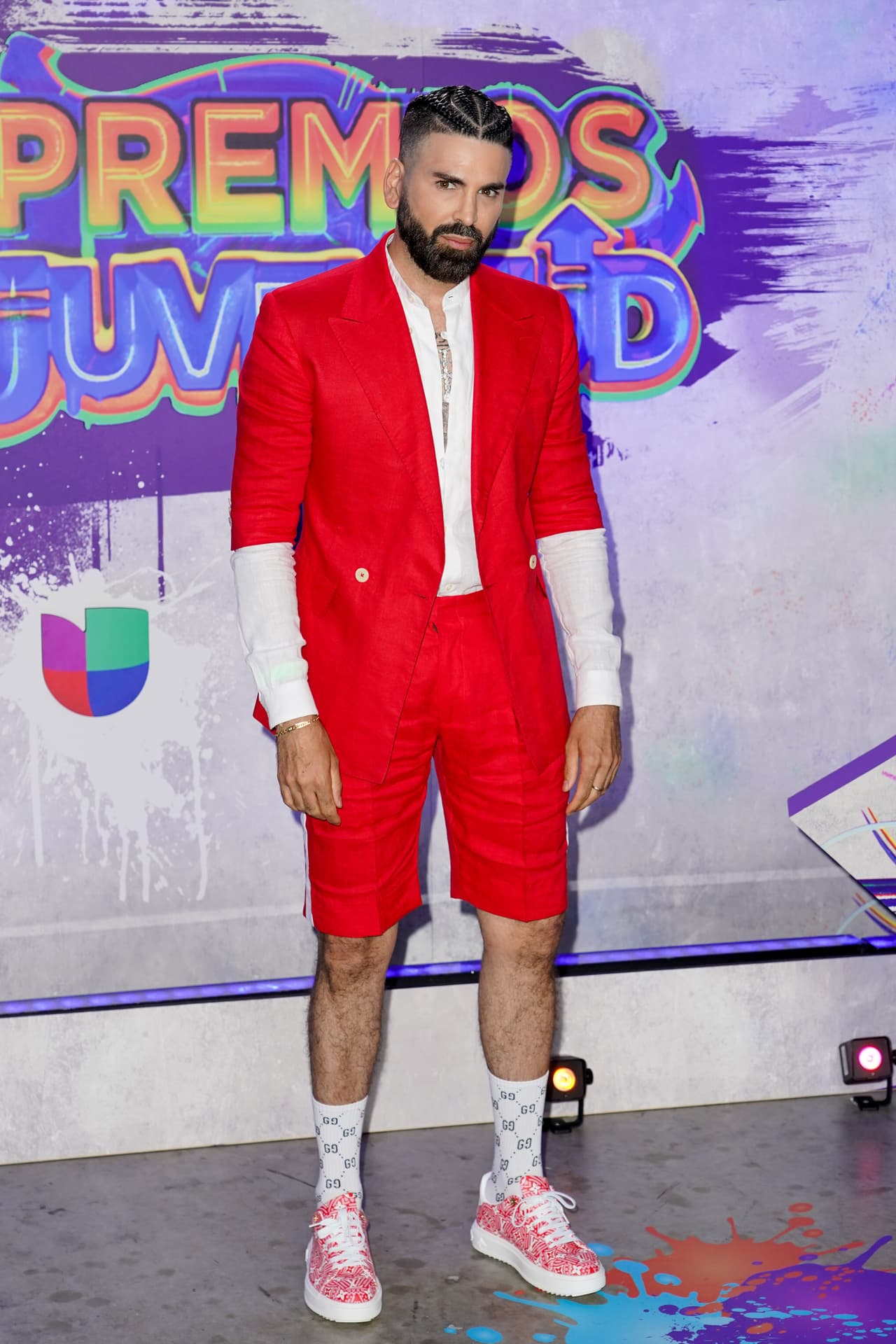 El presentador eligió un conjunto color rojo, formado por un pantalón corto y un saco con manga tres cuartos, que complementó con una camisa blanca y tenis rosas.