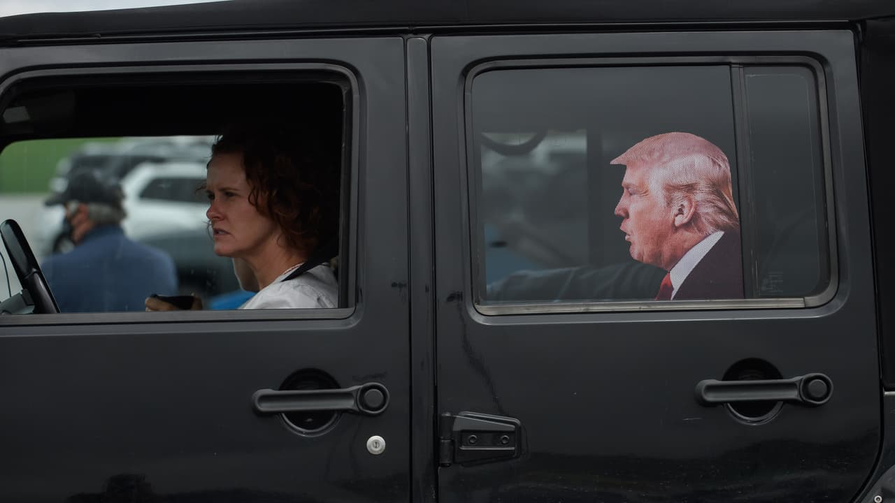 Una simpatizante de 
<a href="https://www.univision.com/temas/donald-trump">Trump</a> llega a un estacionamiento para abordar un autobús de enlace antes del evento de campaña en el Aeropuerto Regional Arnold Palmer. En la ventanilla del asiento trasero tiene pegada una imagen del presidente, que parece viajar como pasajero.