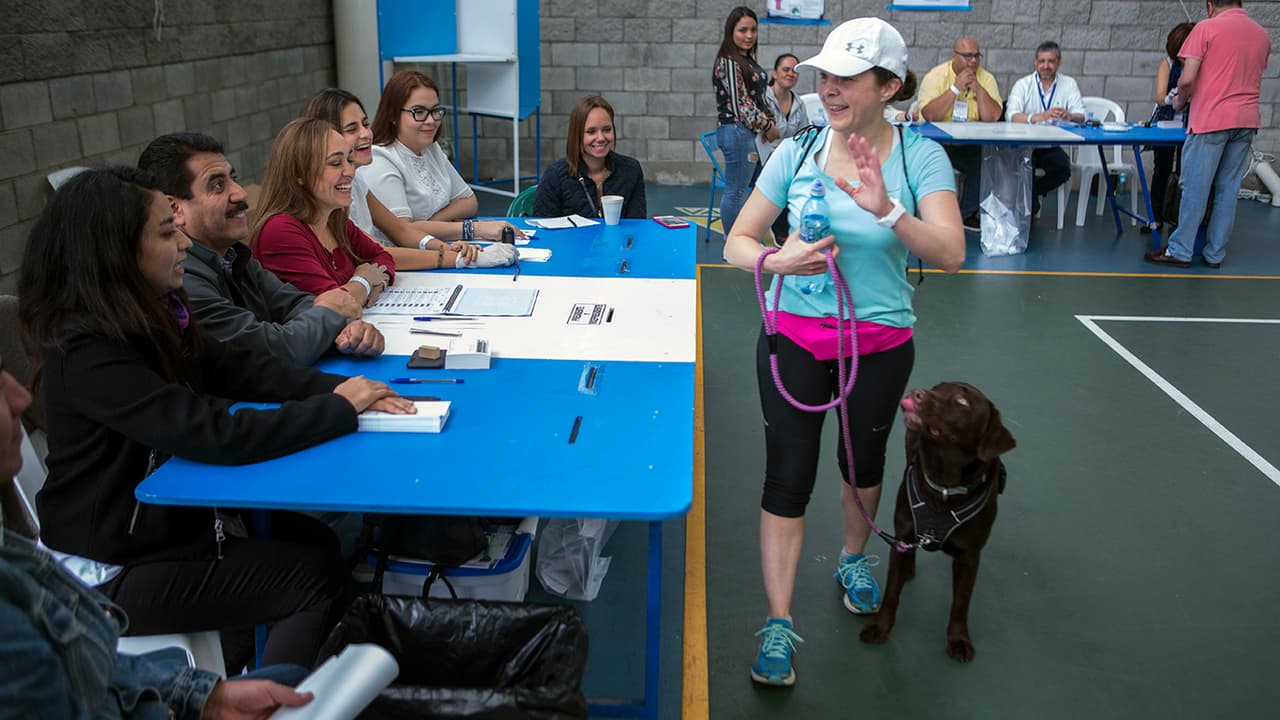 Una mujer saluda a los funcionarios electorales mientras camina con su perro tras emitir su voto en la ciudad de Guatemala.