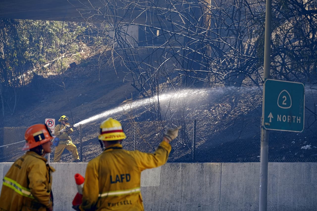 Bomberos lanzan agua el domingo 19 de junio de 2016 en una ladera sobre la Carretera Estatal Ruta 2 después de que un incendio de maleza se extendió amenazando casas en Los Ángeles. Bomberos de Los Ángeles dijeron que controlaron el incendio en el barrio densamente poblado ubicado a lo largo de una autopista. (AP Foto/Richard Vogel)