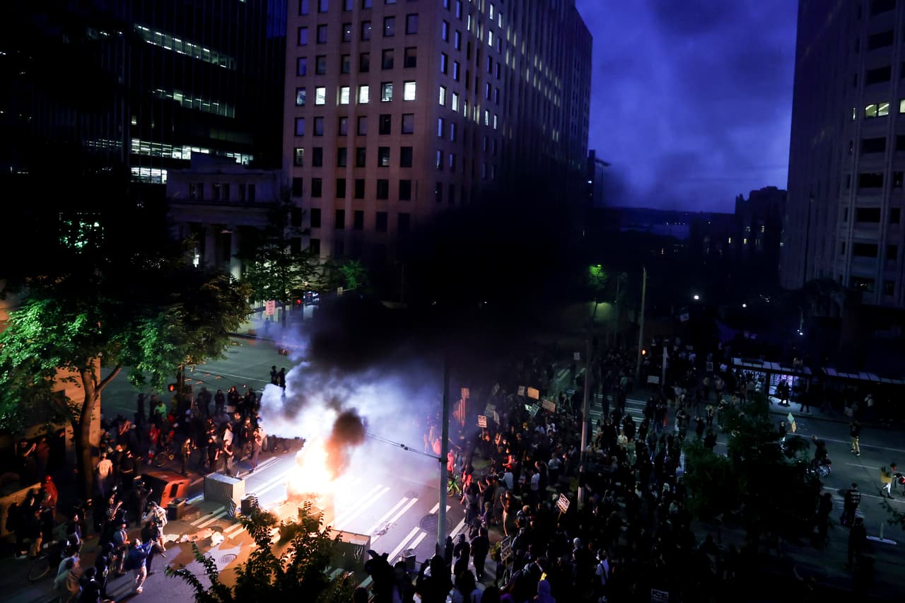 Manifestantes rodean un contenedor de basura incendiado frente al Edificio Federal Henry M. Jackson durante una protesta contra los arrestos por inmigración federal, el miércoles 11 de junio de 2025, en Seattle.