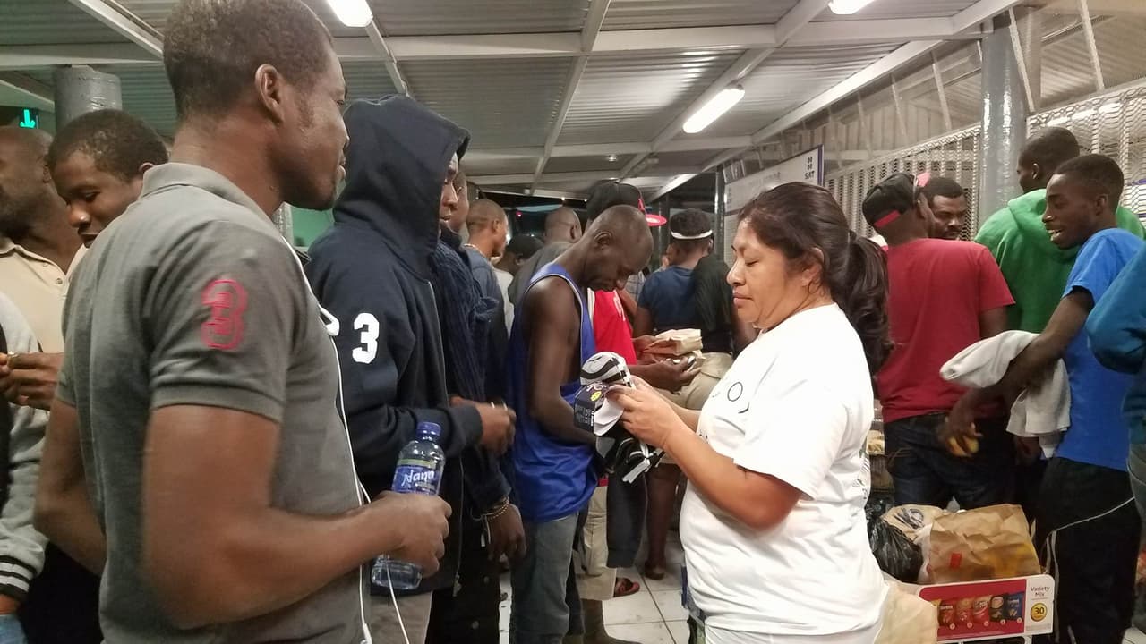 Alma Mendoza entrega calcetines a los haitianos que esperan en la garita DeConcinni ser procesados para ingresar al país.