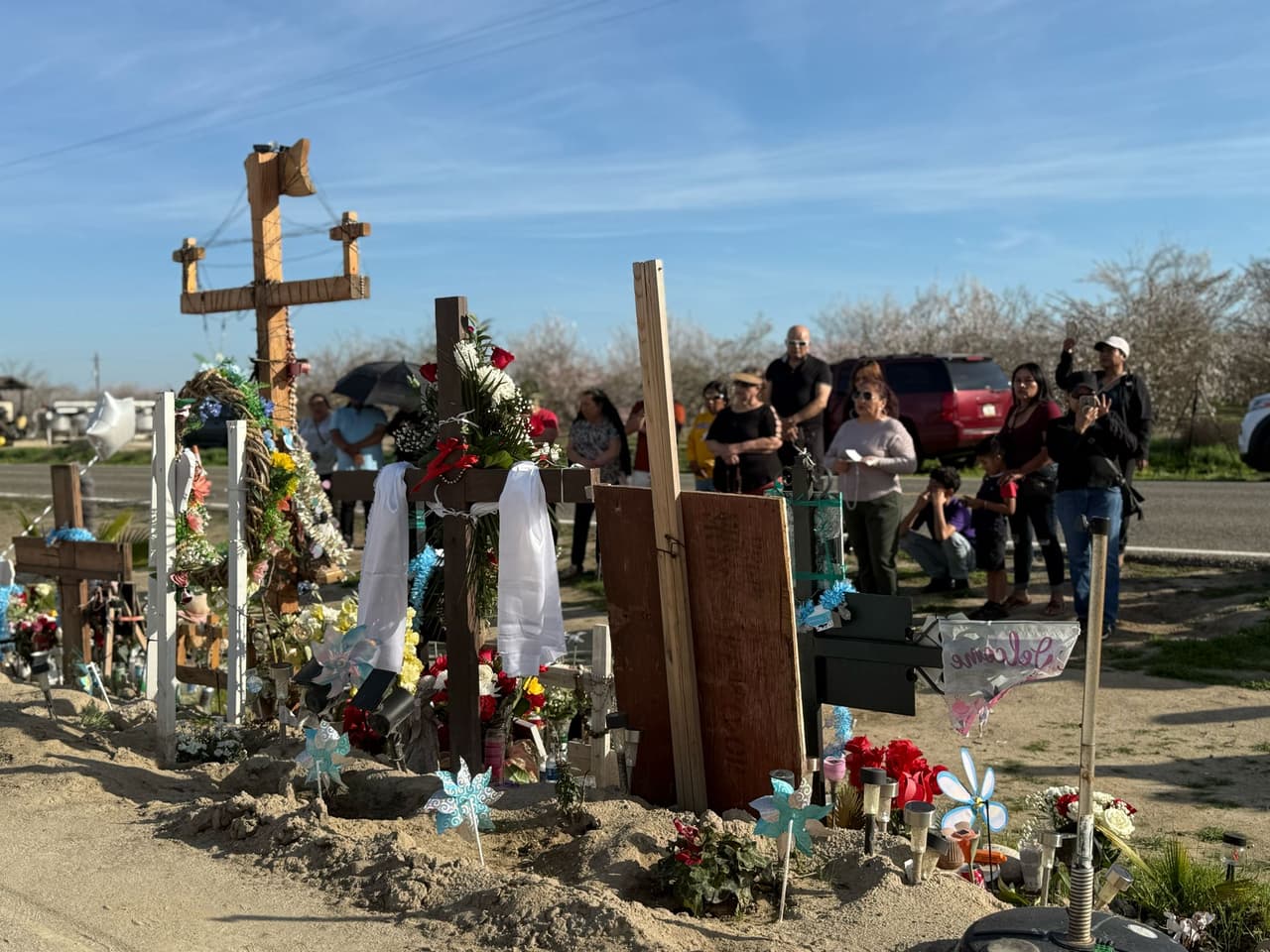 <b>Tributo colectivo:</b> Veladores, flores y ofrendas personales decoran el memorial improvisado en la Avenue 7 de Madera, simbolizando el respeto y cariño de una comunidad que no olvida a sus trabajadores agrícolas caídos en el trágico accidente ocurrido cerca de las 6:00 a.m. de aquel fatídico día de 2024.