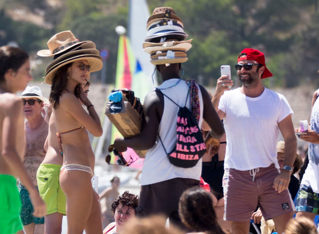 Alessandra Ambrosio lleva más de una semana en las playas de Ibiza disfrutando del verano español. Aquí, la modelo de 36 años bromea con un vendedor de sombreros en la playa.