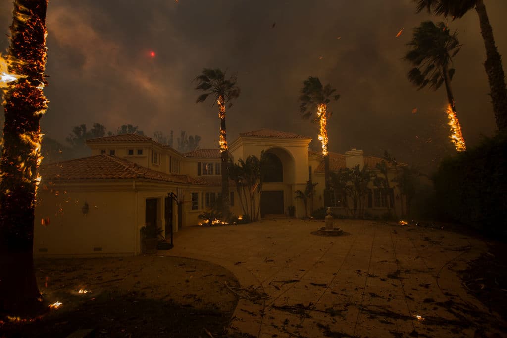 Las llamas caen de palmas ardientes y el sol se oculta por el humo encima de una casa en medio del incendio de Woolsey en Malibu. David McNew/Getty Images