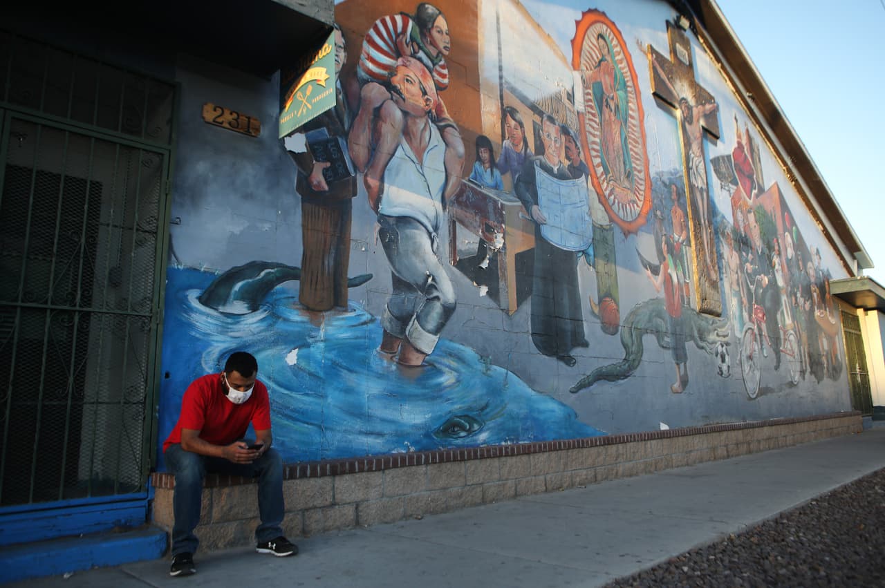 Un hombre con mascarilla espera sentado frente a un mural en El Paso, Texas. Es una de las ciudades con mayor porcentaje de población latina (
<a href="https://www.census.gov/quickfacts/fact/table/elpasocountytexas/RHI725219#qf-headnote-a" target="_blank">un 92% de acuerdo con estimaciones del censo de Estados Unidos</a>). Más de la mitad de los 20,000 fallecimientos registrados en Texas por la pandemia son de origen hispano, 
<a href="https://covid.cdc.gov/covid-data-tracker/#cases_casesinlast7days" target="_blank">según datos de los CDC</a>.