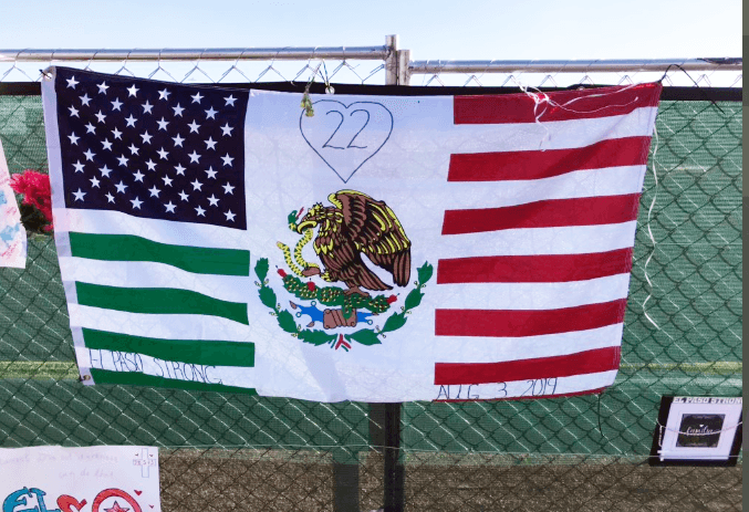 Una bandera mezcla los elementos y colores de las banderas de México y Estados Unidos. En el centro está el número 22, que era la cifra de fallecidos en el ataque hasta abril de este año, que murió la víctima número 23 del atentado: Guillermo "Memo" García.
