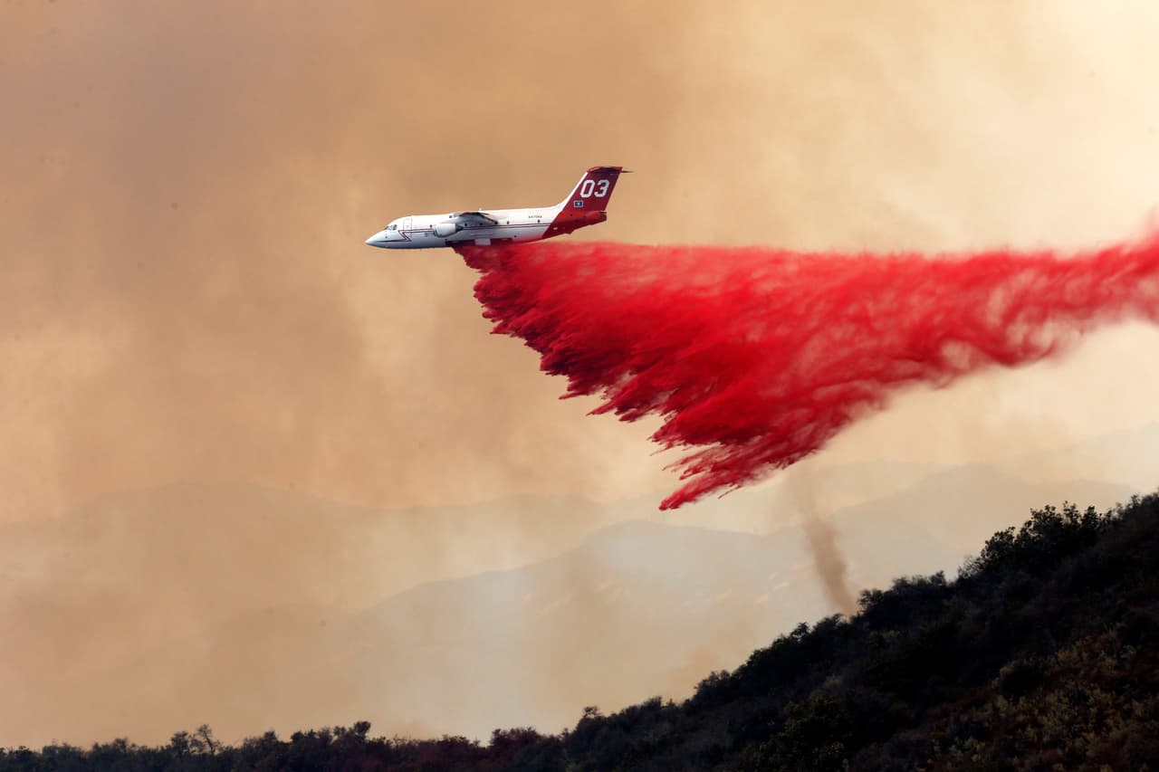 Avión arroja químico para retardar la propagación del fuego.