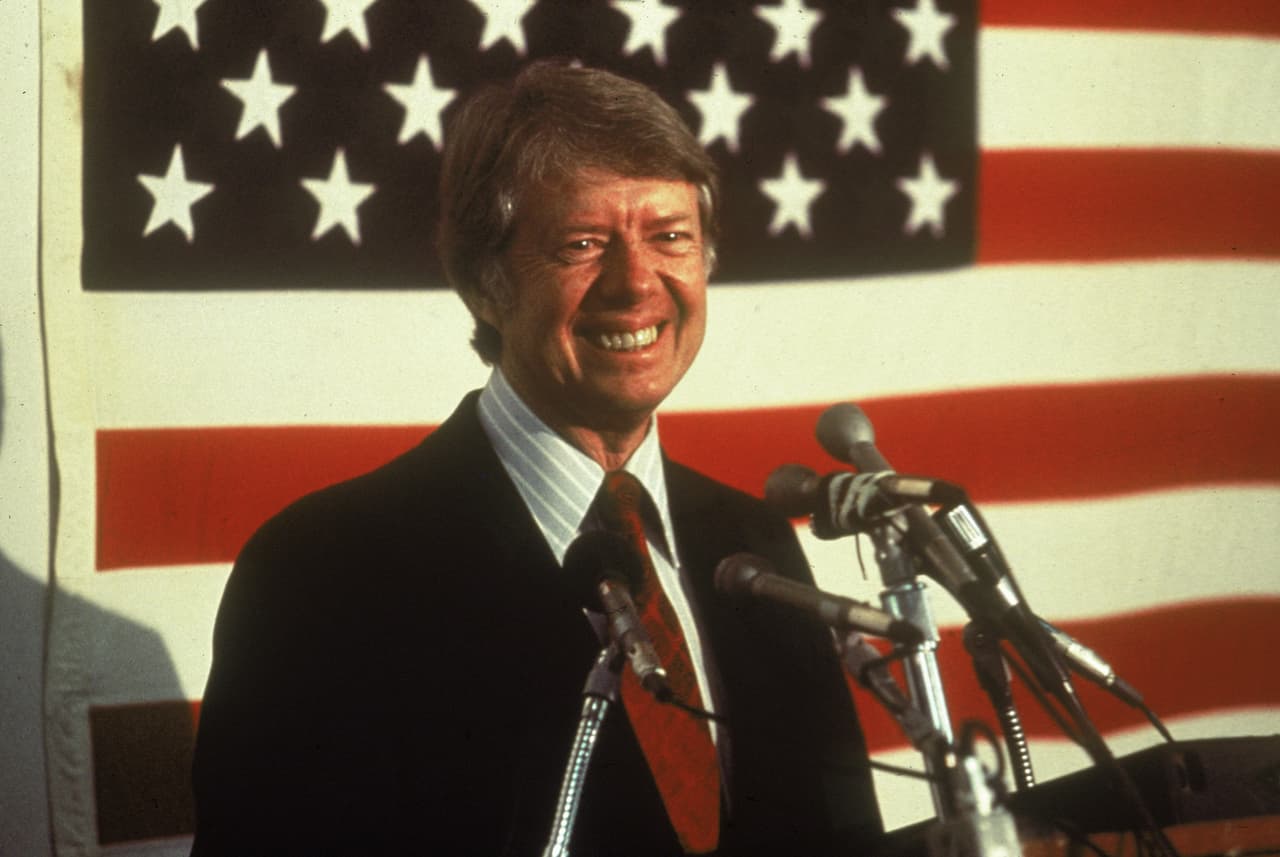 U.S. president Jimmy Carter smiling at a podium in front of an American flag, 1970s. (Photo by Hulton Archive/Getty Images)