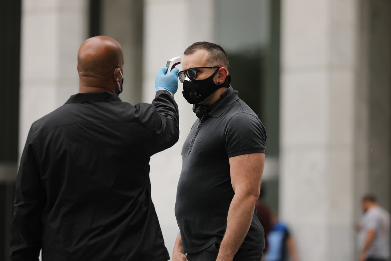 Un empleado de Apple revisa la temperatura de un cliente antes de entrar a la tienda de la quinta Avenida que abrió sus puertas a los clientes bajo el sistema de citas para varios servicios.