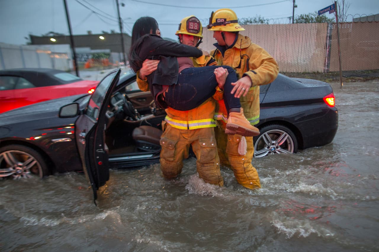 Un bombero carga a una mujer cuyo auto terminó atrapado en una corriente de agua en el vecindario de Sun Valley, en Los Ángeles.