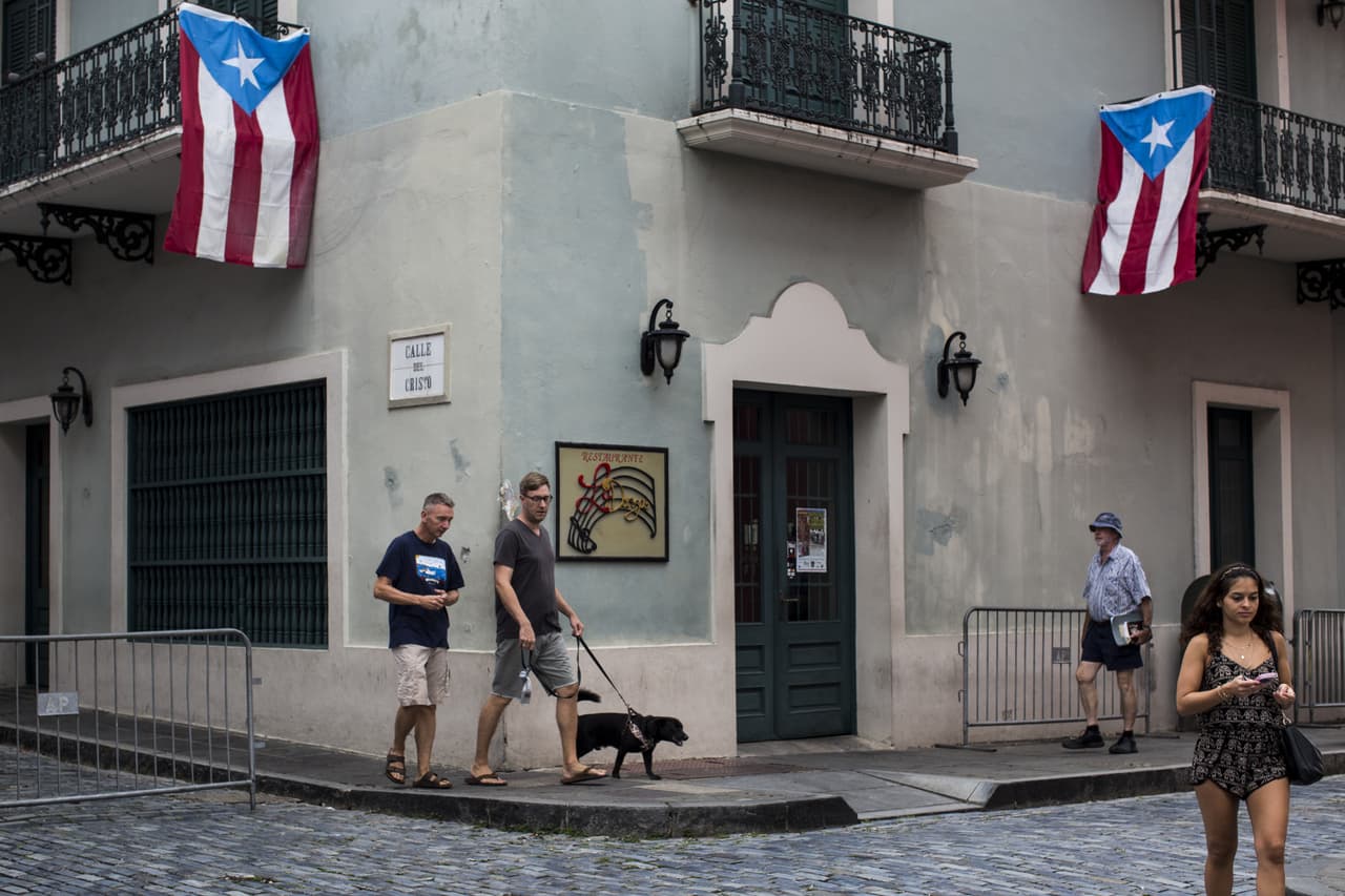 Peatones pasan bajo banderas de Puerto Rico que cuelgan de balcones en San Juan. 1 de mayo de 2016.