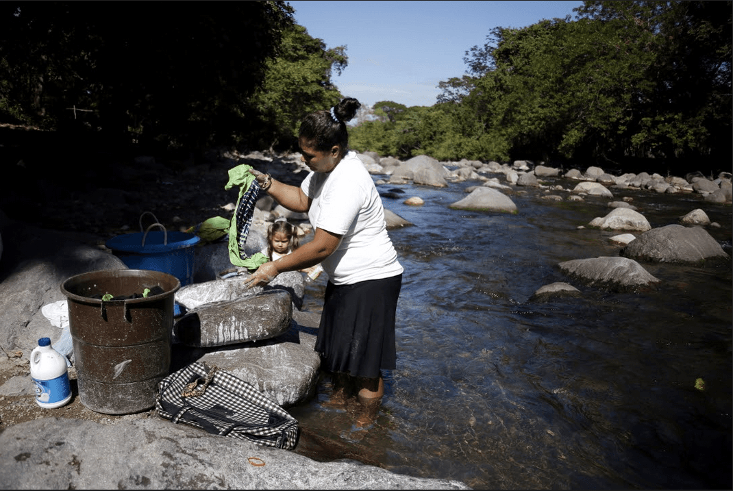 Carmen washes a women's soccer uniform in the community of Guapinol while her youngest daughter plays by her side, in the river. Carmen was a member of the resistance to the mining project and her husband emigrated to the United States when the conflict broke out.