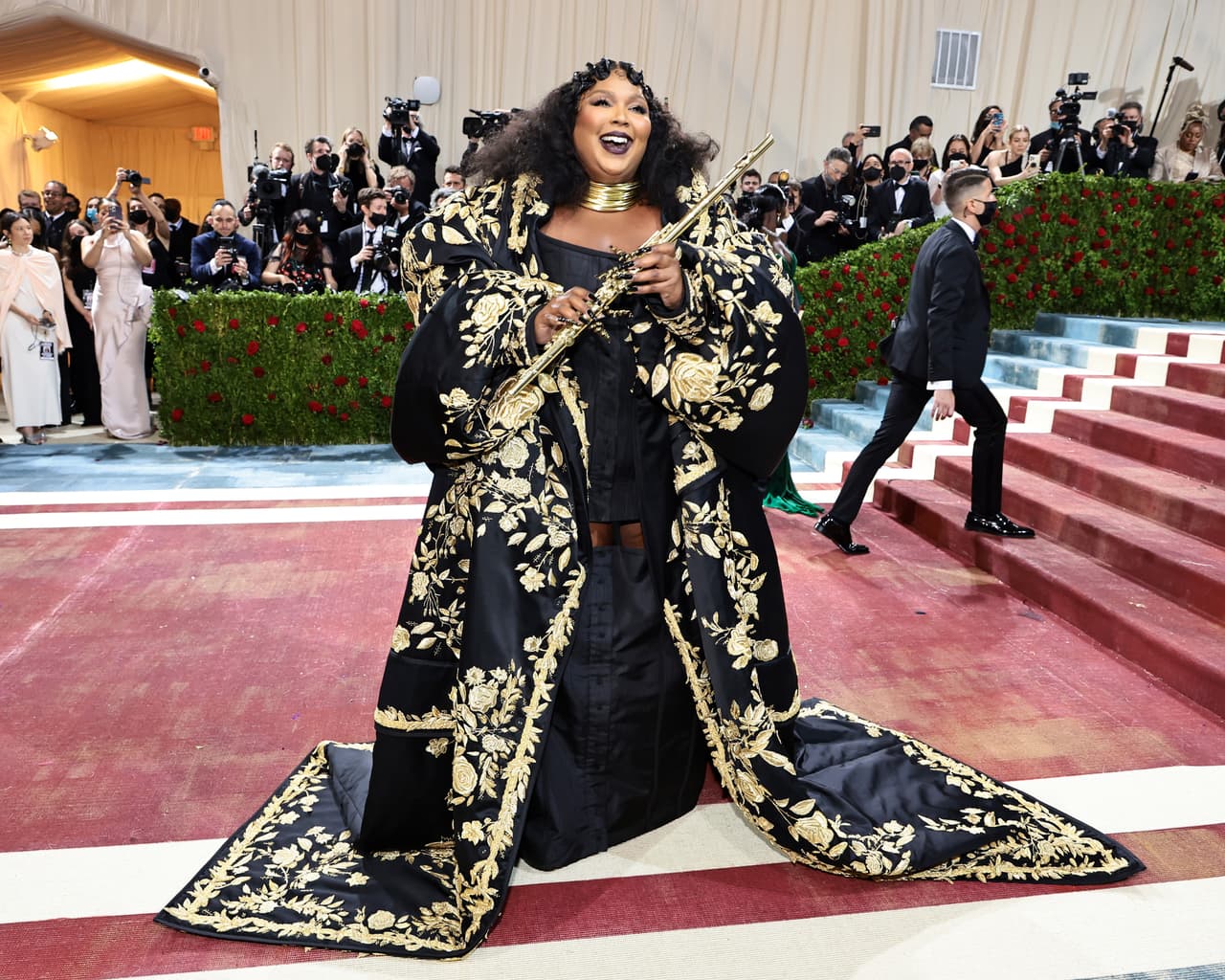 La cantante 
<b>Lizzo</b> también tomó inspiración de la abundancia económica de la llamada ‘Gilded Age’. Para la ocasión, lució un vestido negro con una gran capa de acabados dorados, cada uno bordado a mano, del diseñador Tom Browne.
