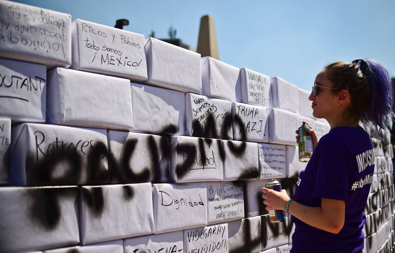 Un activista escribe la palabra 'Racismo' en un muro simulado durante una marcha anti-Trump en la Ciudad de México.