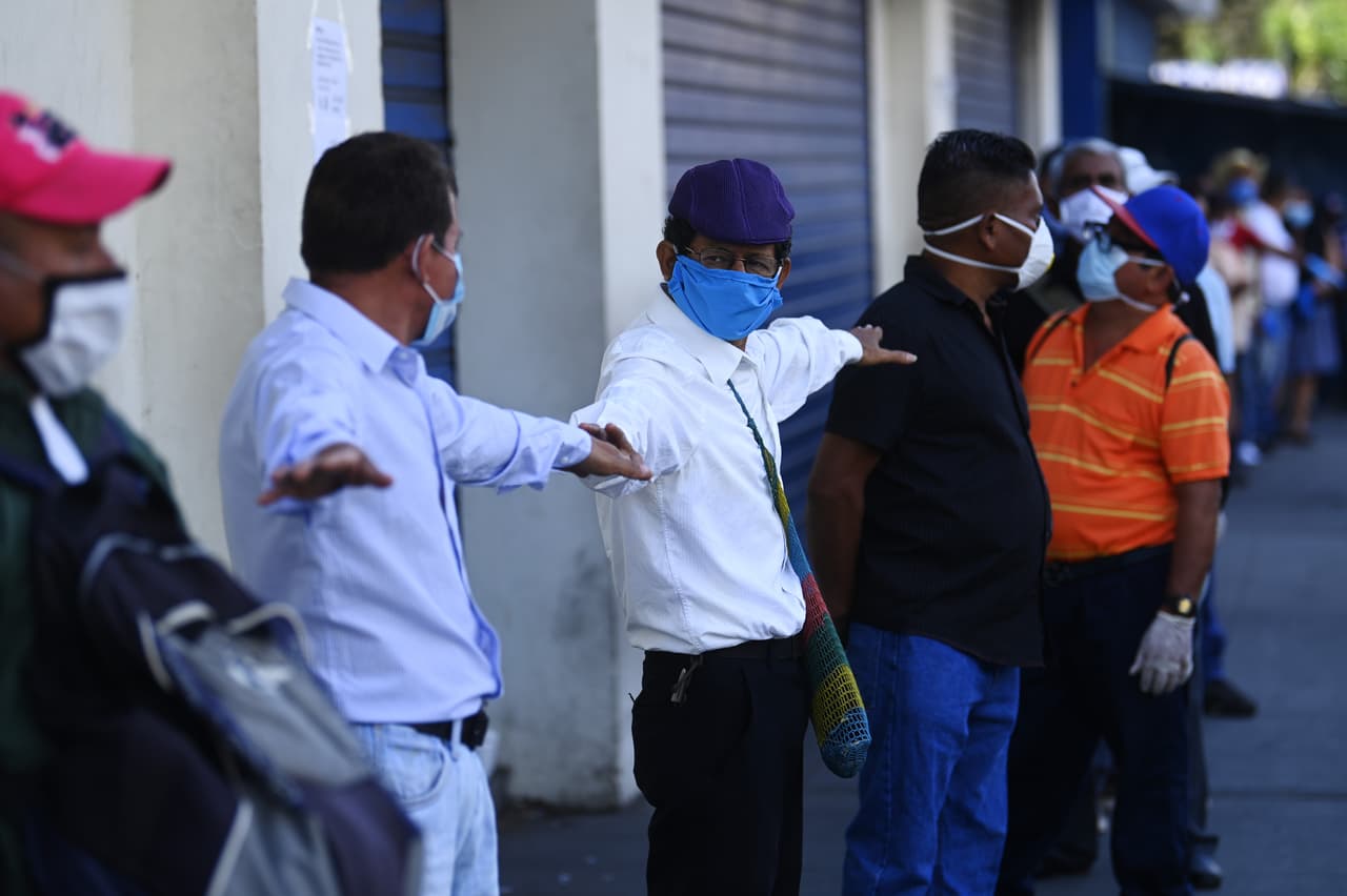 Pensionistas con mascarillas hacen fila delante de un banco de San Salvador.