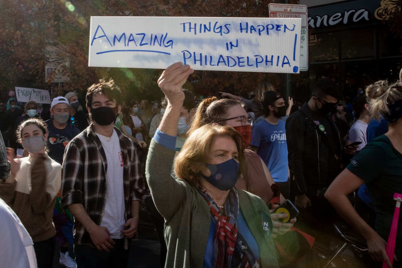 La gente celebra fuera del Centro de Convenciones de Filadelfia después de que Joe Biden fuera declarado ganador de las elecciones presidenciales de 2020 el 7 de noviembre de 2020 en Filadelfia, Pensilvania. La manifestante sostiene un cartel que lee "
<b>Suceden cosas asombrosas en Filadelfia</b>", en referencia a las expresiones del presidente Trump durante el primer debate presidencial, “
<a href="https://www.univision.com/local/philadelphia-wuvp/elecciones-estados-unidos-2020/cosas-malas-pasan-en-filadelfia-la-acusacion-de-trump-durante-el-debate-presidencial">cosas malas pasan en Filadelfia</a>” .