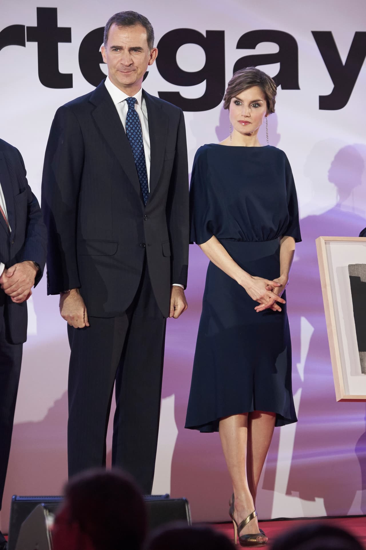 Aunque a la Reina le gustan los vestidos más ajustados a su silueta, en ocasiones apuesta por trajes de evocaciones más románticas con más vuelo y caída como este azul oscuro de cuello bandeja de la diseñadora mallorquina Cortana.