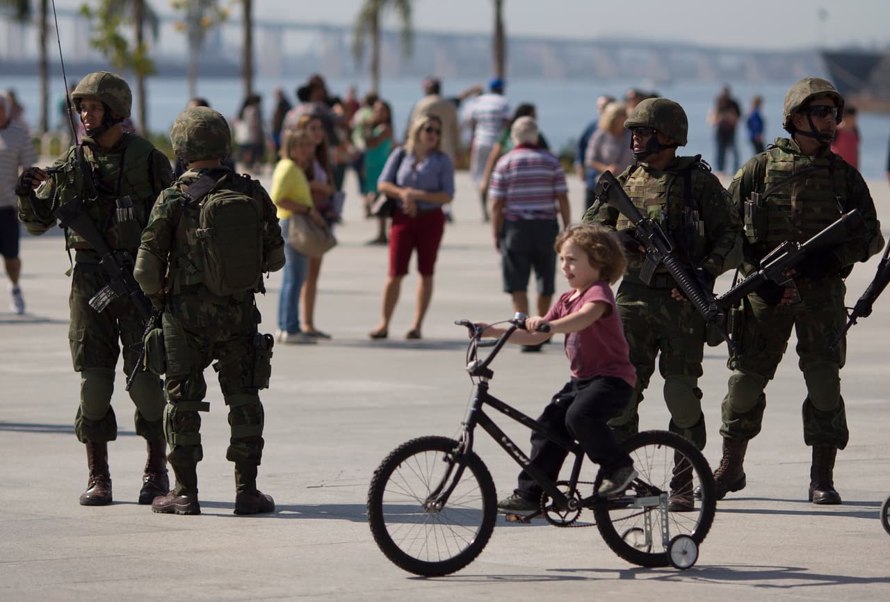 Un niño conduce una bicicleta mientras soldados resguardan la plaza Maua en Río de Janeiro, Brasil, el sábado 9 de julio de 2016, durante el despliegue de seguridad para que conozcan las áreas que deberán patrullar durante los Juegos Olímpicos. (AP Foto/Leo Correa)