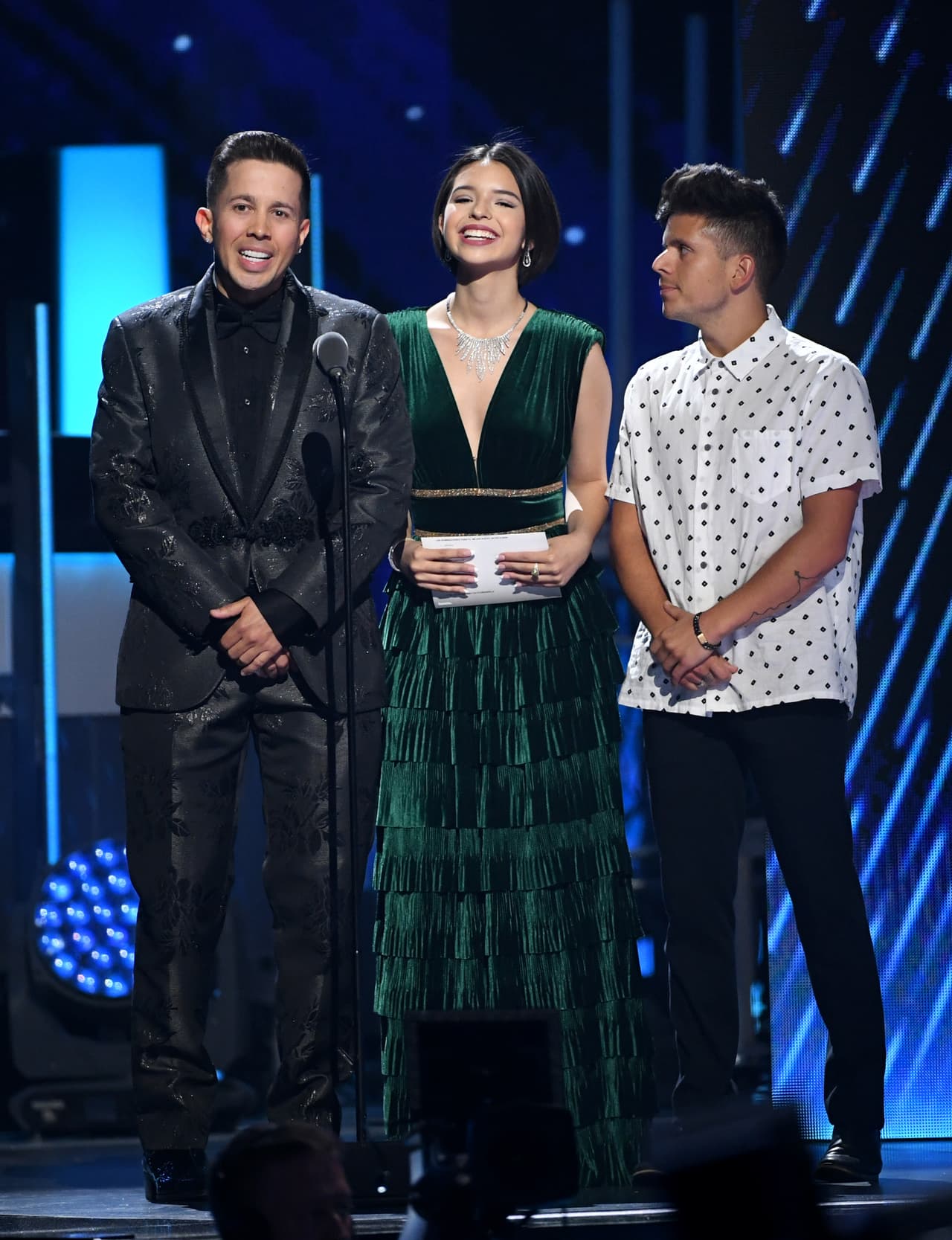 Una vez en el escenario, acompañada de Rudy Mancuso y De La Ghetto, Ángela cambió su vestido: dejó el cuello de tortuga y eligió uno en el mismo tono, pero esta vez con un escote profundo y un colgante que llenó su cuello de luz.