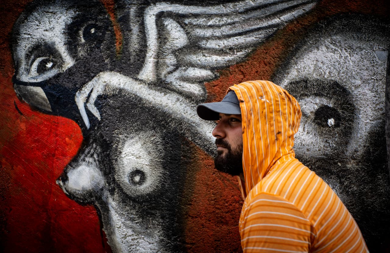 Yulier P. posa junto a su obra, pintada en una pared de La Habana y titulada "El miedo a la Salvacion", en la que, según el artista, quiso expresar la impotencia de la humanidad ante esta pandemia.