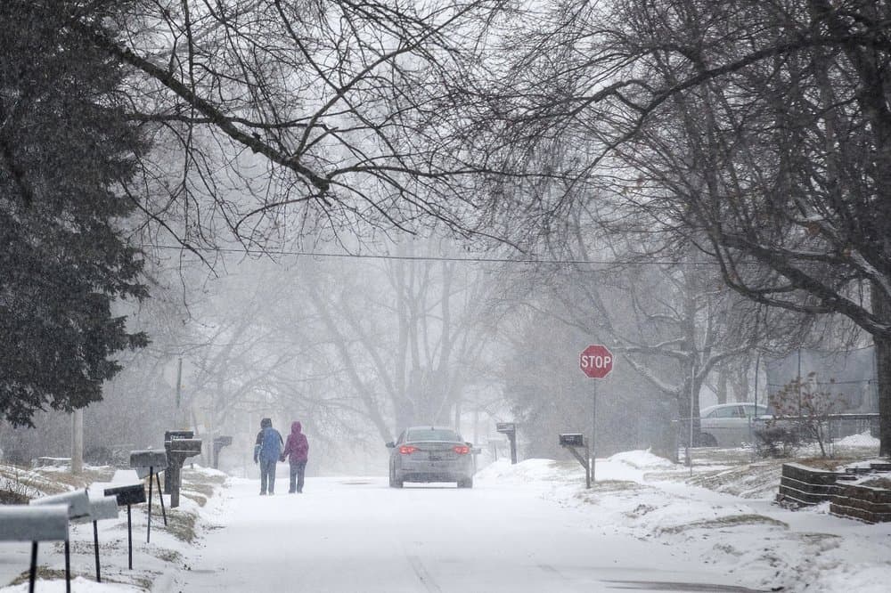 Dos personas se toman de la mano mientras caminan hacia el sur en la calle Madison hacia la Avenida 27 en Bellevue, Nebraska, durante una advertencia de tormenta invernal el lunes 25 de enero de 2021.