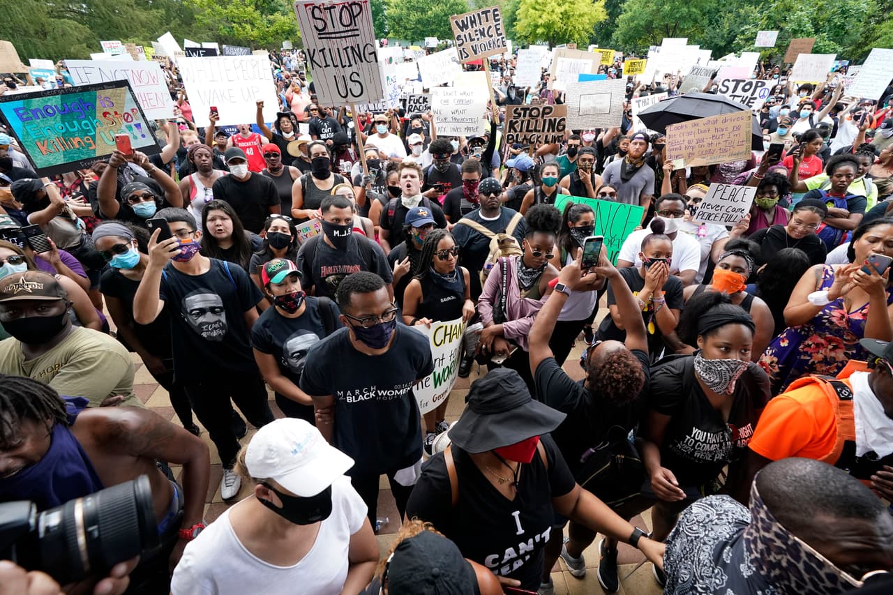 Un grupo de personas, en su mayoría vestidos de negro y con letreros de protesta, se manifiestan en Houston, Texas, en la tarde del martes.