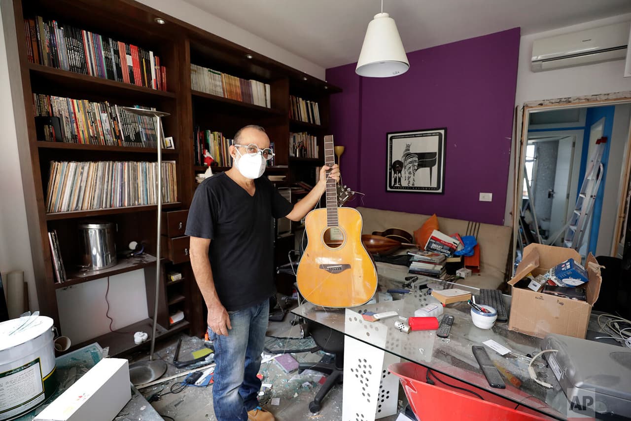 Alain Shoucair, de 38 años, posa mientras sostiene su guitarra rota en lo que queda de su apartamento. 
<b>Dentro de una habitación que funcionaba como estudio, una estantería alcanzó a mantenerse intacta con los artículos y recuerdos musicales de Alain.</b>