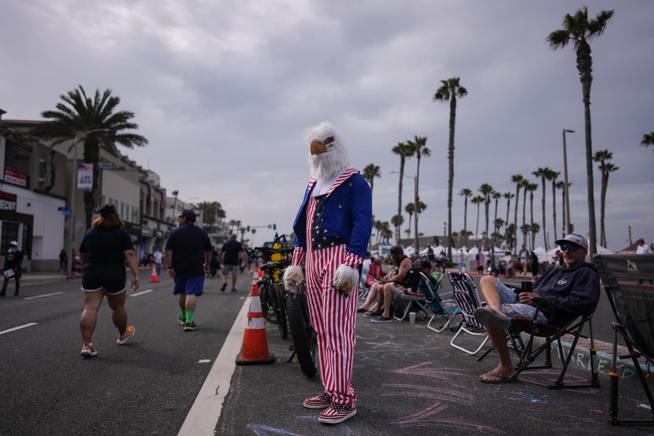 Brian White, vestido con un disfraz de águila calva y ropa con motivos patrióticos de la bandera estadounidense, se encuentra a lo largo del recorrido de un desfile del Día de la Independencia en Huntington Beach, California, el sábado 4 de julio de 2026.
