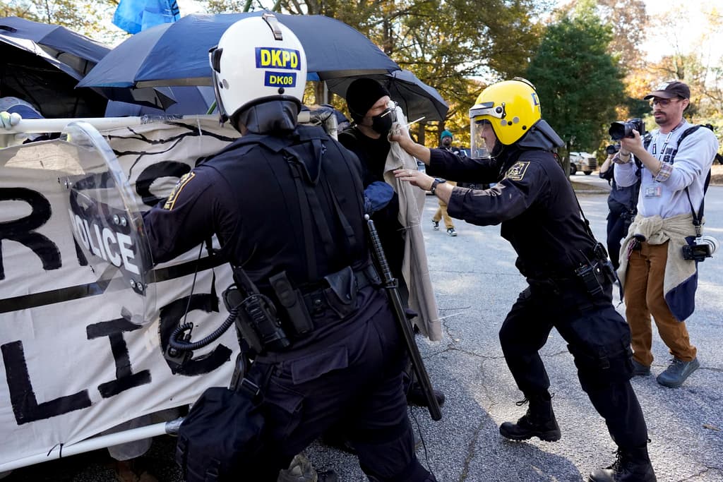 Un grupo de manifestantes, incluidos algunos con máscaras, gafas protectoras y trajes químicos para protegerse contra los gases lacrimógenos, se abalanzó sobre una fila de oficiales con equipo antidisturbios en una calle afuera del centro de entrenamiento.