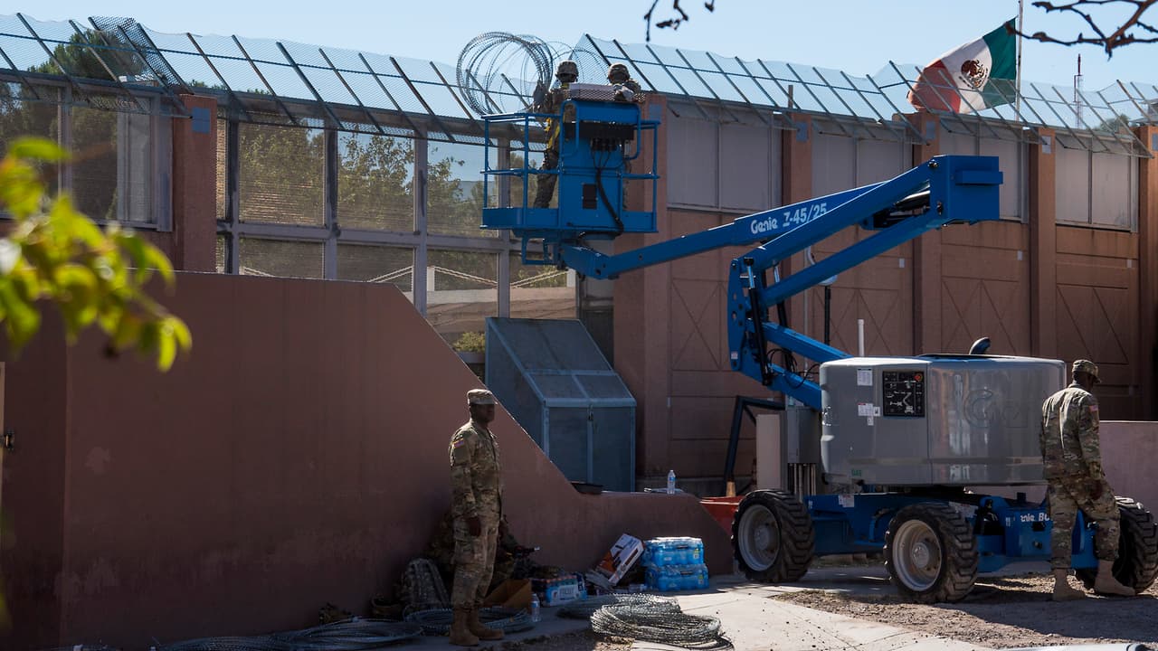 Dos soldados instalan alambre para prevenir que personas intenten saltar ante la posible llegada de la caravana de migrantes centroamericanos.