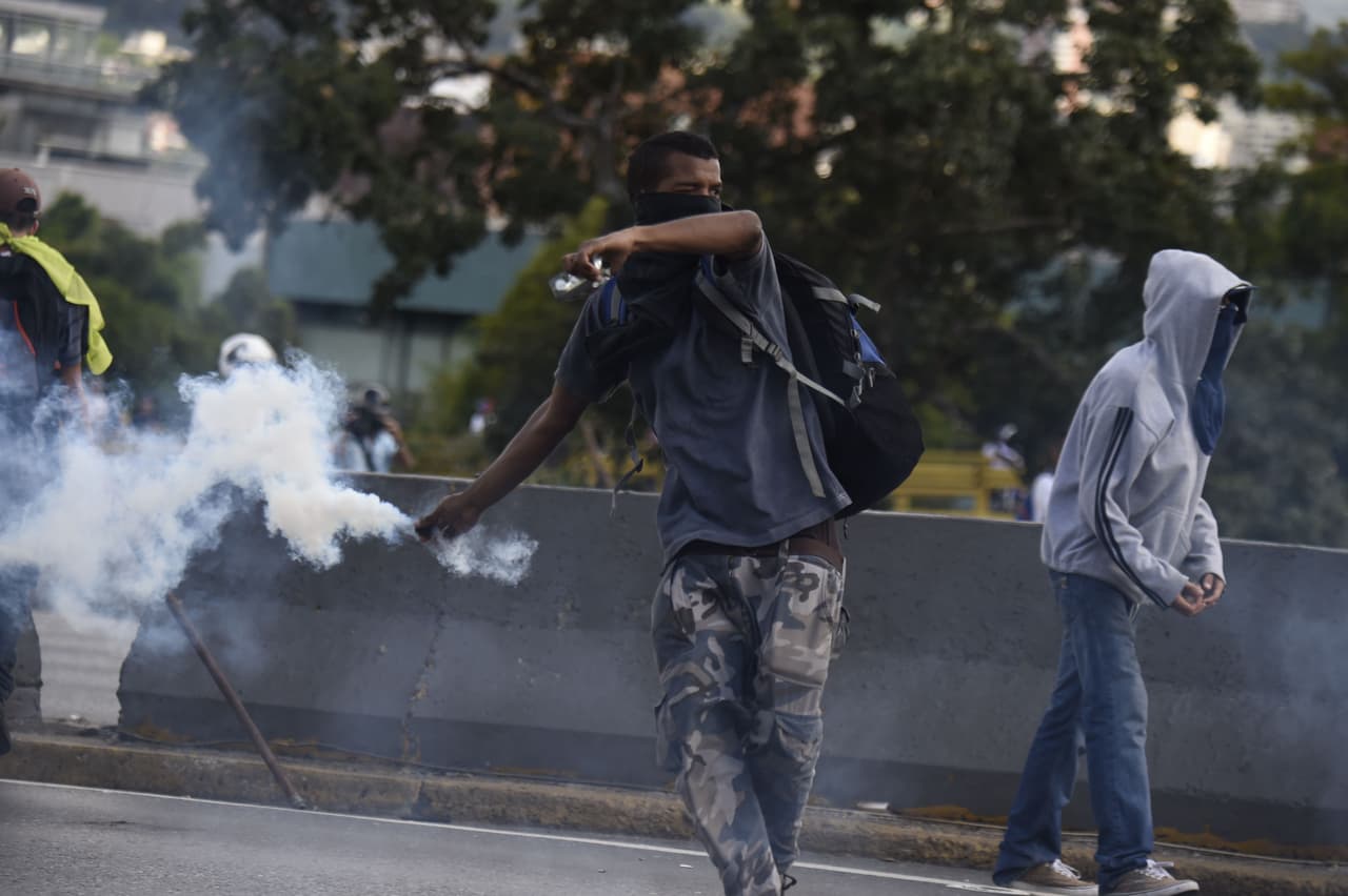 Un manifestante regresa a la policía antidisturbios una bomba lacrimógena, en una de las concentraciones que ha sido obstaculizada por la fuerza pública, hacia el centro de Caracas.