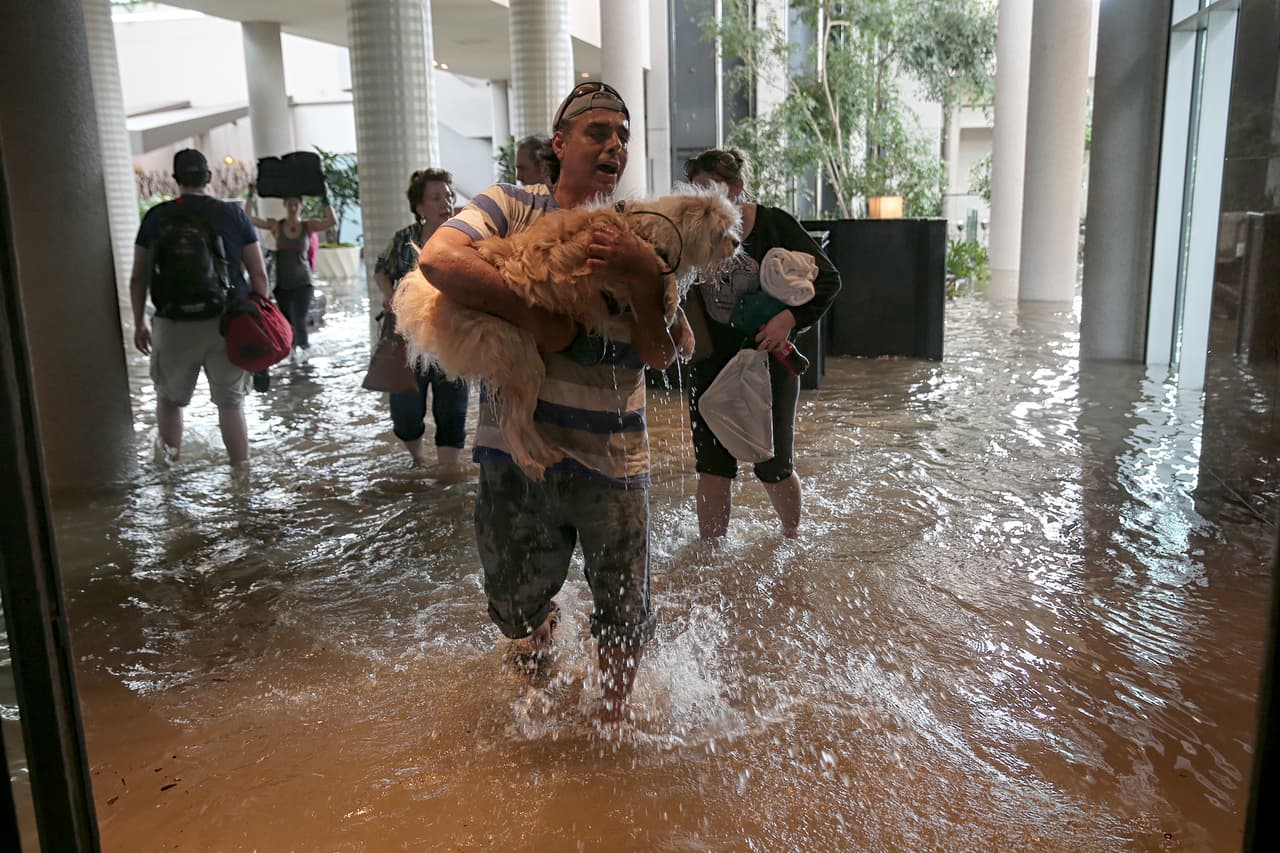 Un afectado entra con su perro en brazos a hotel convertido en refugio, luego del mandato de evacuación obligatoria por la ruptura de la represa Addicks al oeste de Houston.