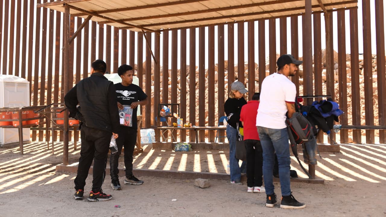 Migrantes que buscan asilo se quitan el polvo de la ropa mientras esperan en una estación de agua para presentarse ante un agente de la Patrulla Fronteriza después de cruzar a EEUU por Yuma.