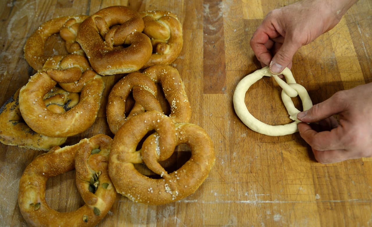 <b>Da forma a los lazos. </b>Una vez que se ha dividido la masa y formado las tiras, toma dos extremos de un lazo. Cruza los extremos por encima dos veces y después aprieta en cada lado del lazo; repetir con cada tira de masa y ponerlos en una placa de hornear ligeramente enharinada y tapa con un paño de cocina. Deja que fermente durante unos 45 minutos, hasta que dupliquen su tamaño. 
<b>Si prefieres hacer los lazos duros y crujientes, elimina esta fermentación</b> y pasa directamente al siguiente paso. 
<br>
<br>
<br>