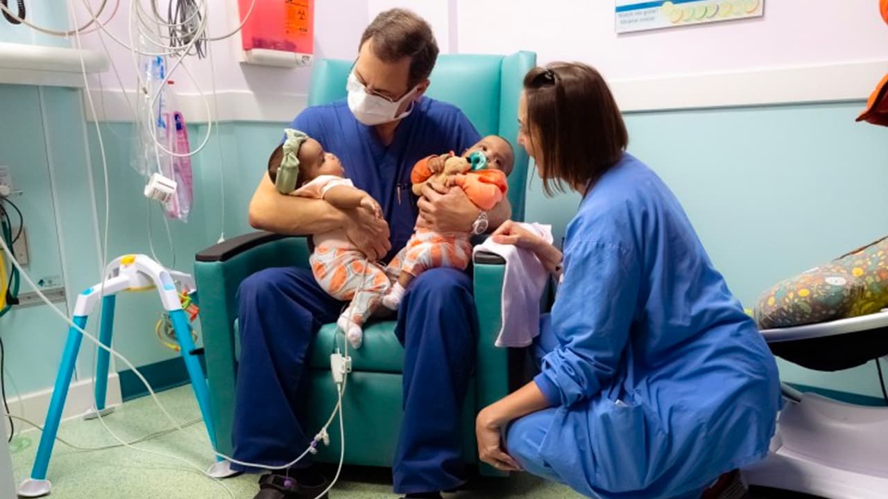 El pediatra José Iglesias lleva en sus brazos a las gemelas, en compañía de la doctora Fran Lynch.